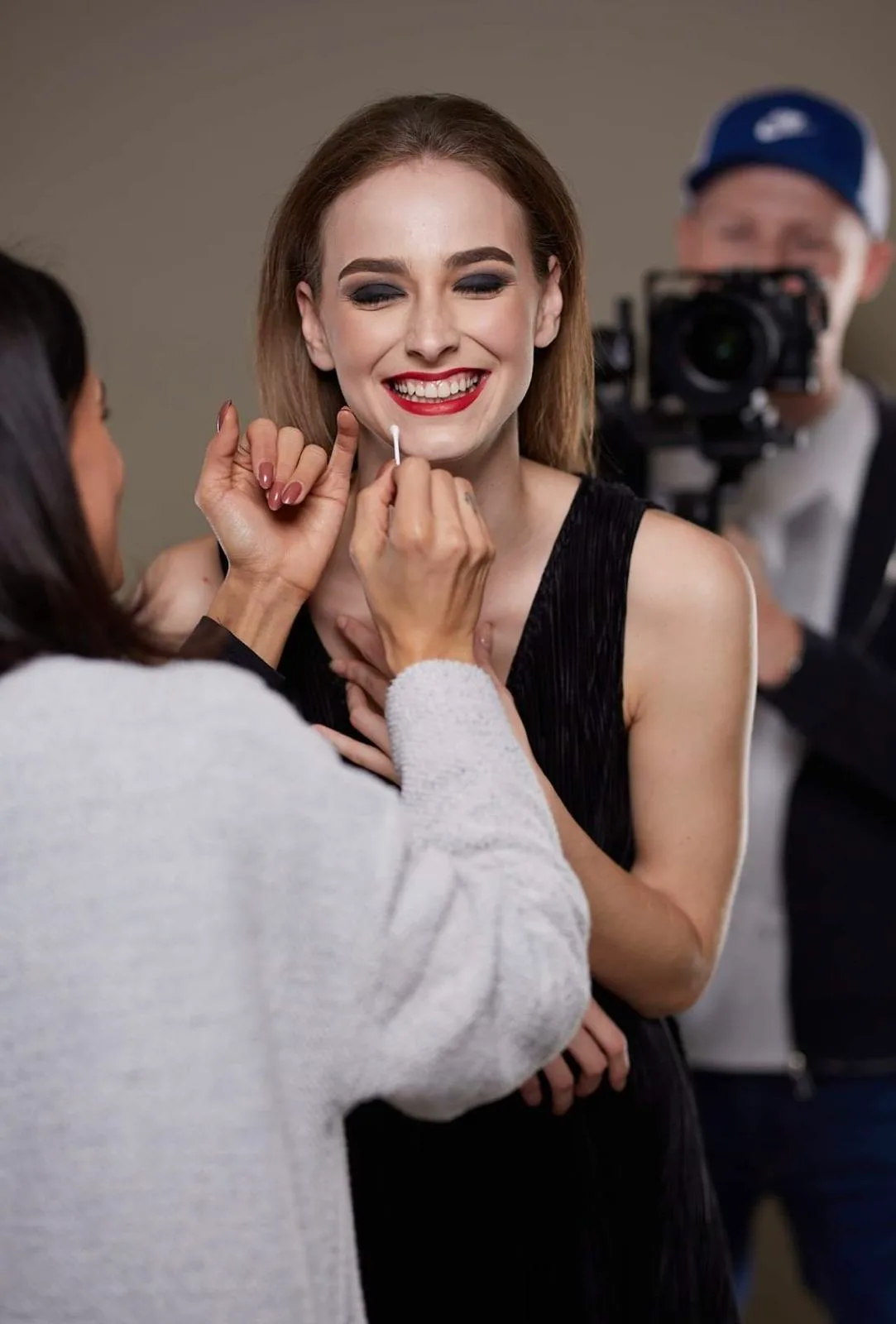 Vizážistka dokončuje červený rúž modelke počas fotografovania.